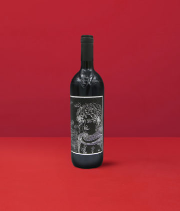 Une élégante bouteille de Capo di Stato Loredan Gasparini Venegazzu IGT avec son étiquette artistique sur un fond rouge