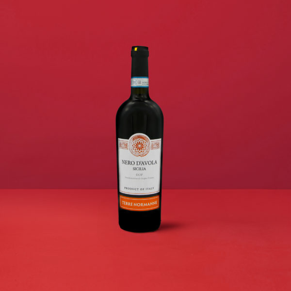 Bouteille de Nero d'Avola - Terre Normanne DOP reflétant le rouge intense et les reflets grenat caractéristiques du vin sicilien.